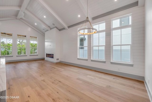 unfurnished living room featuring light wood finished floors, lofted ceiling with beams, a glass covered fireplace, and an inviting chandelier