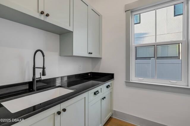 kitchen with baseboards, a sink, dark countertops, white cabinets, and wood finished floors