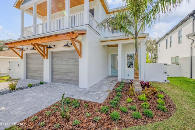 view of front of house with fence, an attached garage, a balcony, decorative driveway, and a gate