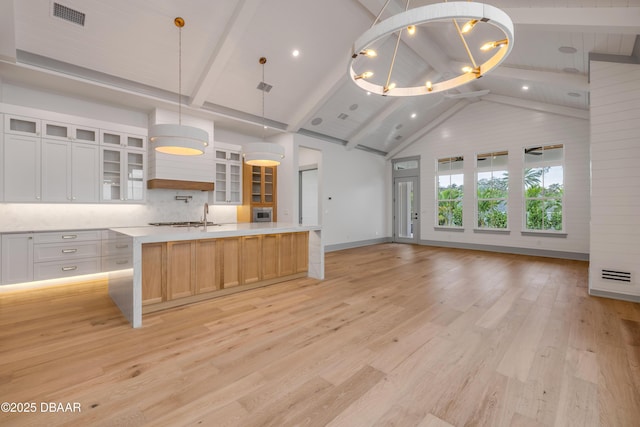 kitchen with an island with sink, light countertops, light wood finished floors, open floor plan, and visible vents