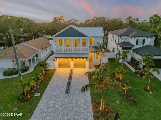 raised beach house featuring fence, metal roof, decorative driveway, a garage, and a lawn
