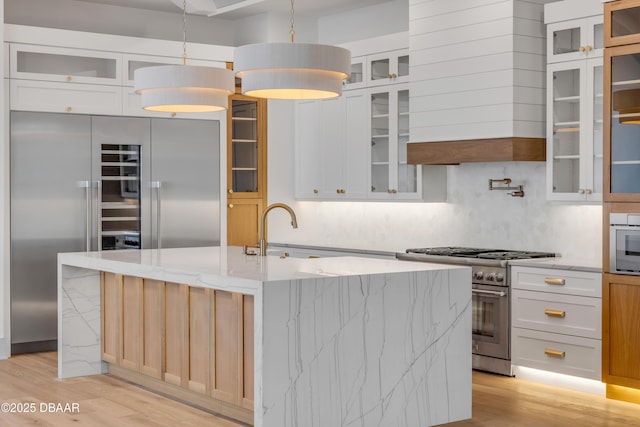 kitchen featuring high end appliances, light wood-style flooring, a sink, and light stone countertops
