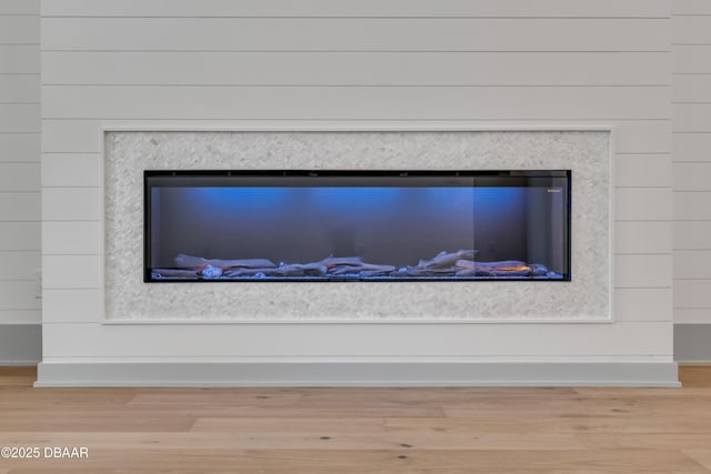 room details featuring baseboards, wood finished floors, and a glass covered fireplace