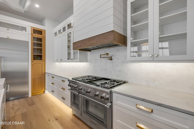 kitchen featuring white cabinetry, premium appliances, light stone countertops, and custom range hood