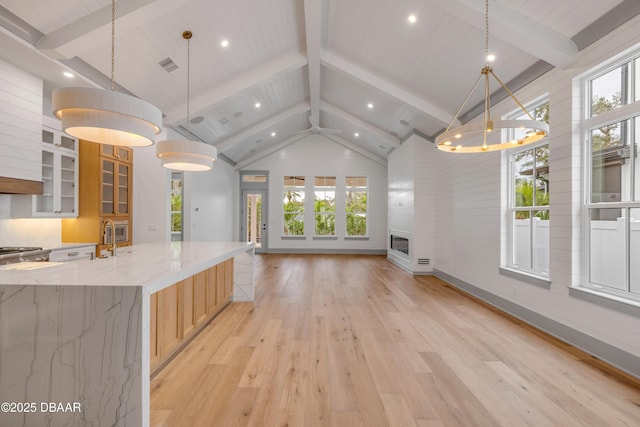 kitchen featuring open floor plan, decorative light fixtures, light wood-type flooring, vaulted ceiling with beams, and glass insert cabinets