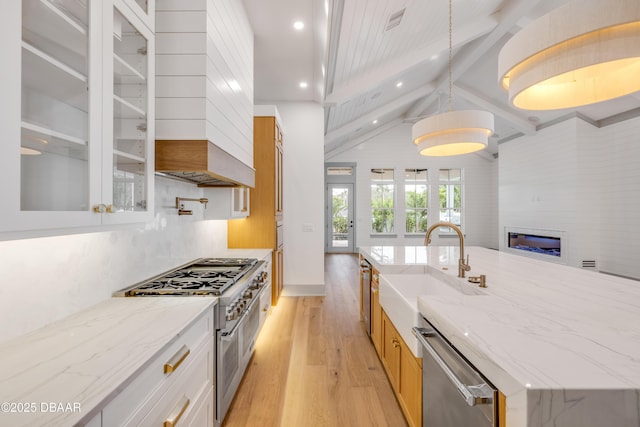 kitchen featuring a sink, light wood-style flooring, light stone countertops, appliances with stainless steel finishes, and glass insert cabinets