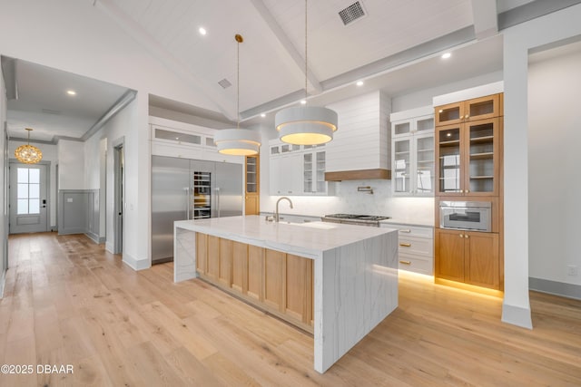 kitchen featuring a large island with sink, a sink, light wood finished floors, and visible vents