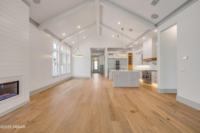 unfurnished living room featuring a sink, beamed ceiling, visible vents, light wood-style flooring, and a glass covered fireplace