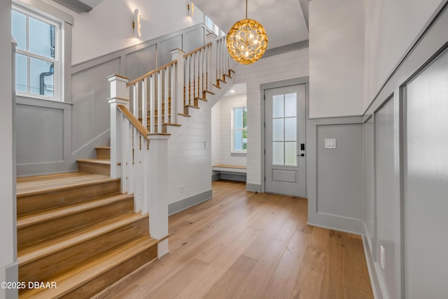 entryway featuring an inviting chandelier, a decorative wall, stairway, and light wood-style flooring