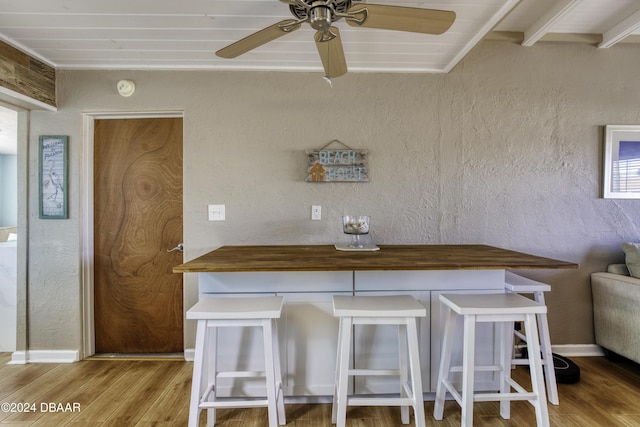 kitchen featuring light hardwood / wood-style floors, ceiling fan, a breakfast bar area, and wooden counters