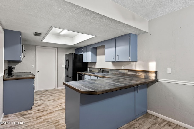 kitchen featuring light hardwood / wood-style flooring, appliances with stainless steel finishes, a textured ceiling, blue cabinets, and kitchen peninsula