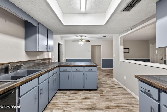 kitchen featuring wood counters, sink, light wood-type flooring, a tray ceiling, and black dishwasher