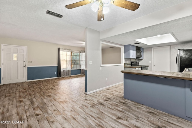 kitchen featuring appliances with stainless steel finishes, tile counters, a textured ceiling, kitchen peninsula, and light wood-type flooring