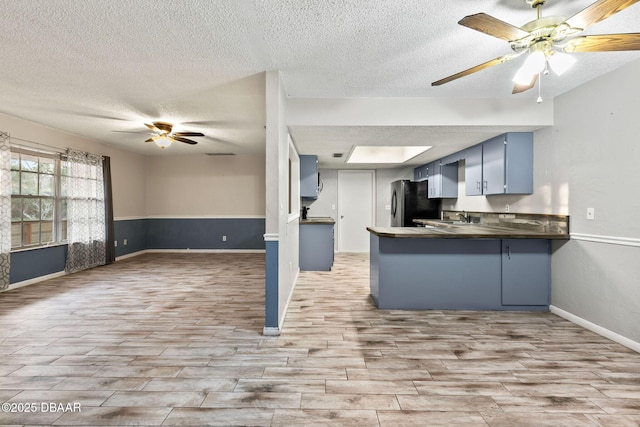 kitchen with black refrigerator, blue cabinets, ceiling fan, kitchen peninsula, and a textured ceiling