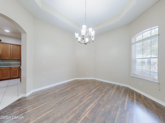 empty room with a tray ceiling, dark hardwood / wood-style flooring, and a notable chandelier