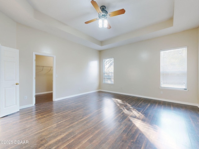 empty room with a raised ceiling, dark wood-type flooring, and ceiling fan