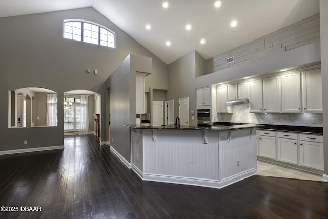 2809 Oakgrove Ave, Saint Augustine, FL 32092 - kitchen featuring arched walkways, under cabinet range hood, a kitchen breakfast bar, high vaulted ceiling, and hardwood / wood-style floors