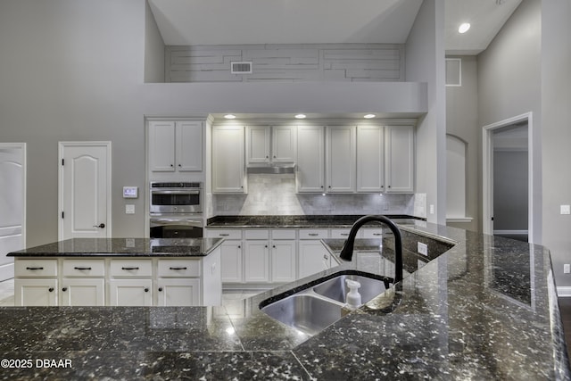 2809 Oakgrove Ave, Saint Augustine, FL 32092 - kitchen featuring double oven, a high ceiling, decorative backsplash, white cabinetry, and under cabinet range hood