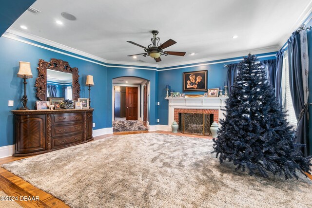 interior space featuring ceiling fan, wood-type flooring, ornamental molding, and a brick fireplace