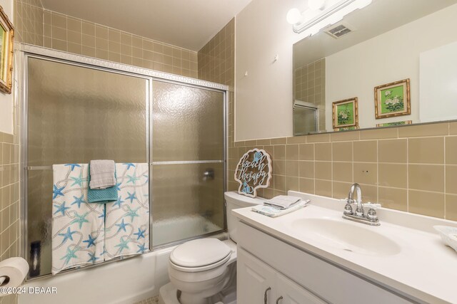 full bathroom with tile walls, enclosed tub / shower combo, vanity, toilet, and decorative backsplash