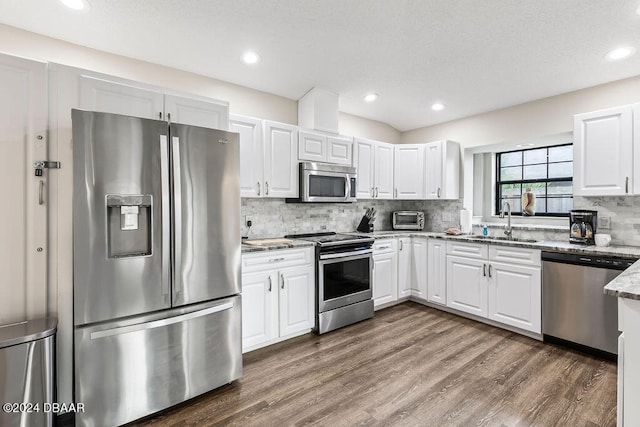 kitchen with light stone counters, stainless steel appliances, white cabinetry, dark hardwood / wood-style floors, and sink