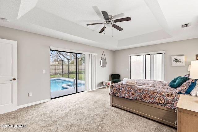 carpeted bedroom featuring access to exterior, ceiling fan, and a tray ceiling