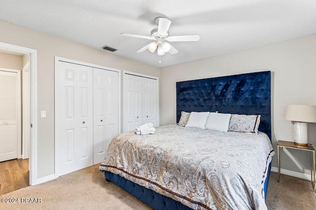 bedroom featuring ceiling fan, two closets, and light colored carpet