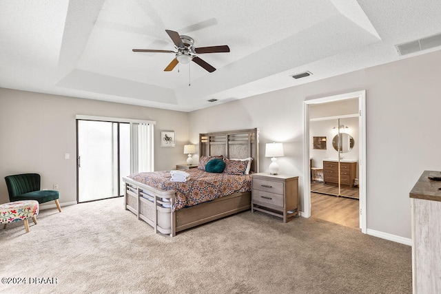 bedroom with a textured ceiling, light carpet, ceiling fan, and a raised ceiling