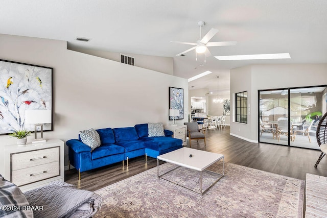 living room with ceiling fan with notable chandelier, dark hardwood / wood-style flooring, and vaulted ceiling with skylight