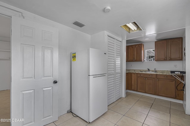 1214 Flomich St, Daytona Beach, FL 32117 - kitchen featuring freestanding refrigerator, light tile patterned flooring, and brown cabinets
