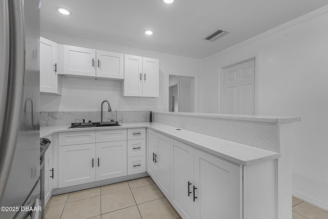 1214 Flomich St, Daytona Beach, FL 32117 - kitchen featuring freestanding refrigerator, white cabinets, light tile patterned flooring, light stone countertops, and a peninsula