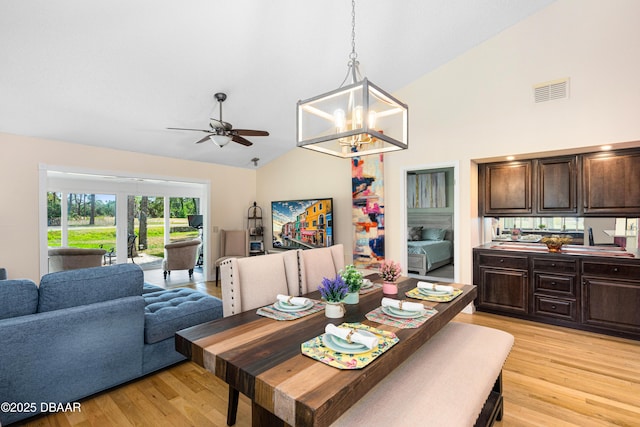 dining space with light wood-style flooring, ceiling fan with notable chandelier, high vaulted ceiling, and visible vents