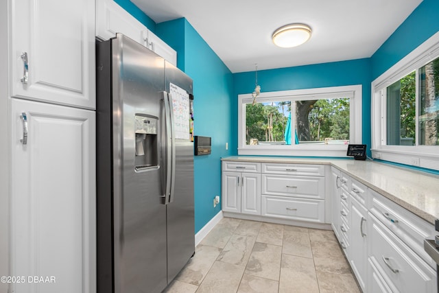 kitchen featuring white cabinets, a wealth of natural light, stainless steel fridge, and light stone counters