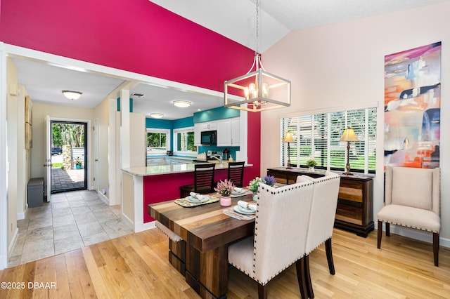 dining space featuring high vaulted ceiling, light wood-style flooring, a notable chandelier, and baseboards