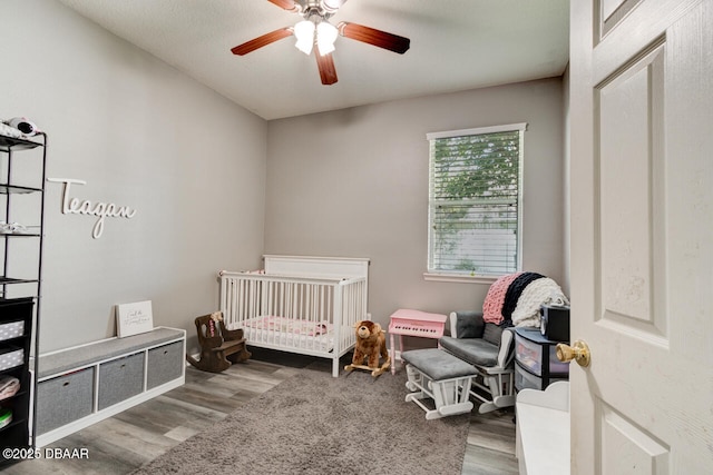 bedroom featuring a crib, wood-type flooring, and ceiling fan