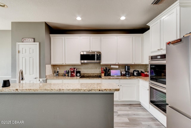 kitchen featuring light stone countertops, appliances with stainless steel finishes, light wood-type flooring, decorative backsplash, and white cabinetry