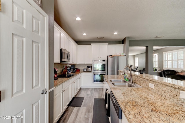 kitchen with white cabinets, sink, light stone countertops, light wood-type flooring, and stainless steel appliances