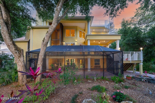 back house at dusk with glass enclosure, a patio, and a balcony