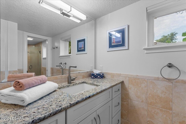 bathroom with vanity, tile walls, a textured ceiling, and a shower with door