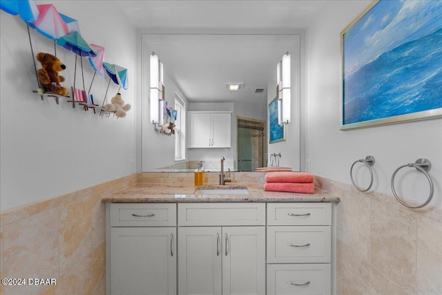 bathroom featuring a shower with door, vanity, and tile walls