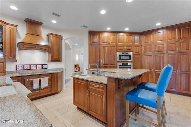 kitchen with light stone countertops, a breakfast bar, sink, and premium range hood