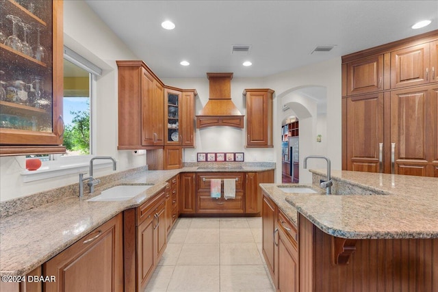 kitchen with custom range hood, sink, light stone counters, and light tile patterned flooring