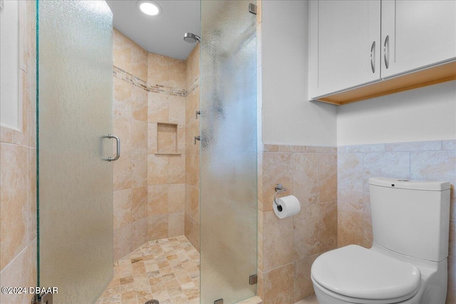 bathroom with toilet, tile walls, and a shower with shower door