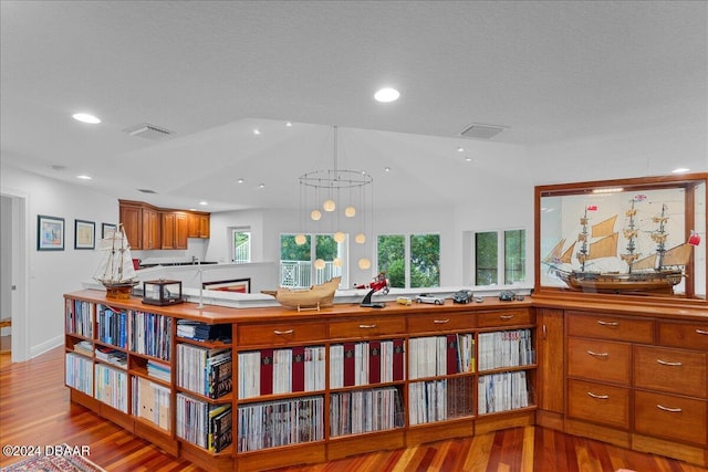 interior space featuring a textured ceiling, hanging light fixtures, a notable chandelier, light wood-type flooring, and vaulted ceiling