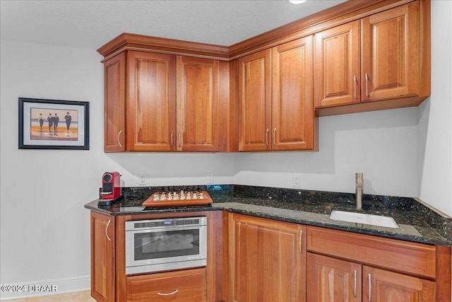 kitchen with dark stone countertops, oven, sink, and a textured ceiling