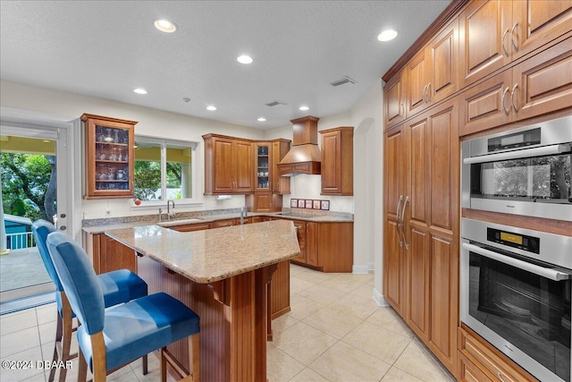 kitchen with a breakfast bar, light stone counters, light tile patterned floors, a kitchen island, and premium range hood