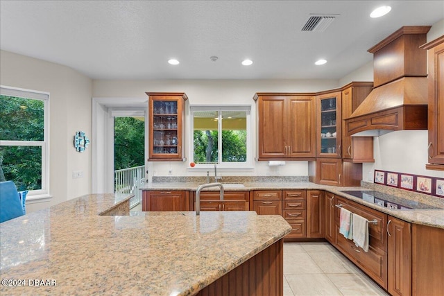 kitchen featuring sink, light stone counters, light tile patterned floors, black electric stovetop, and premium range hood