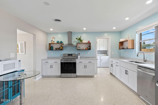 kitchen featuring appliances with stainless steel finishes, sink, washing machine and clothes dryer, white cabinets, and wall chimney exhaust hood