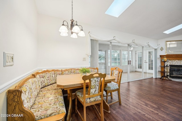 dining area featuring vaulted ceiling with skylight, dark hardwood / wood-style floors, an inviting chandelier, and a tiled fireplace