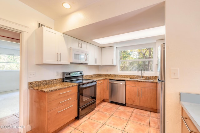 kitchen featuring appliances with stainless steel finishes, white cabinetry, sink, stone countertops, and light tile patterned flooring